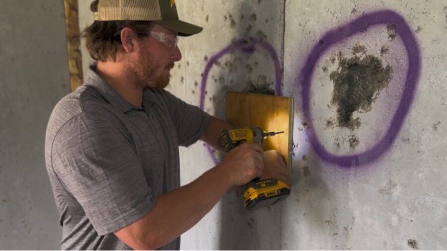 Amidon technician using a rotary drill to prepare a damaged section of a shoot house wall for a ballistic concrete repair patch