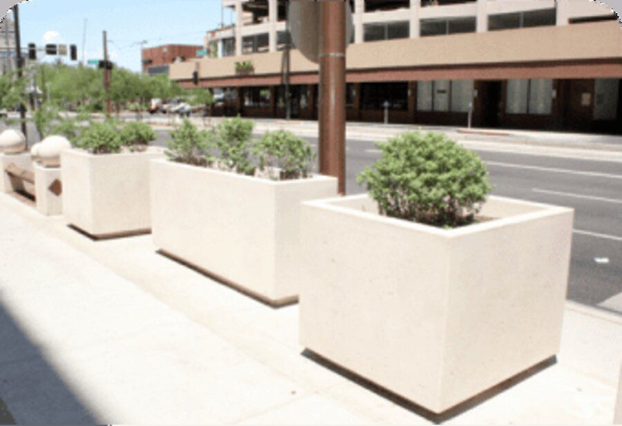 Concrete ballistic flowerpot planters with landscaping along a city sidewalk.
