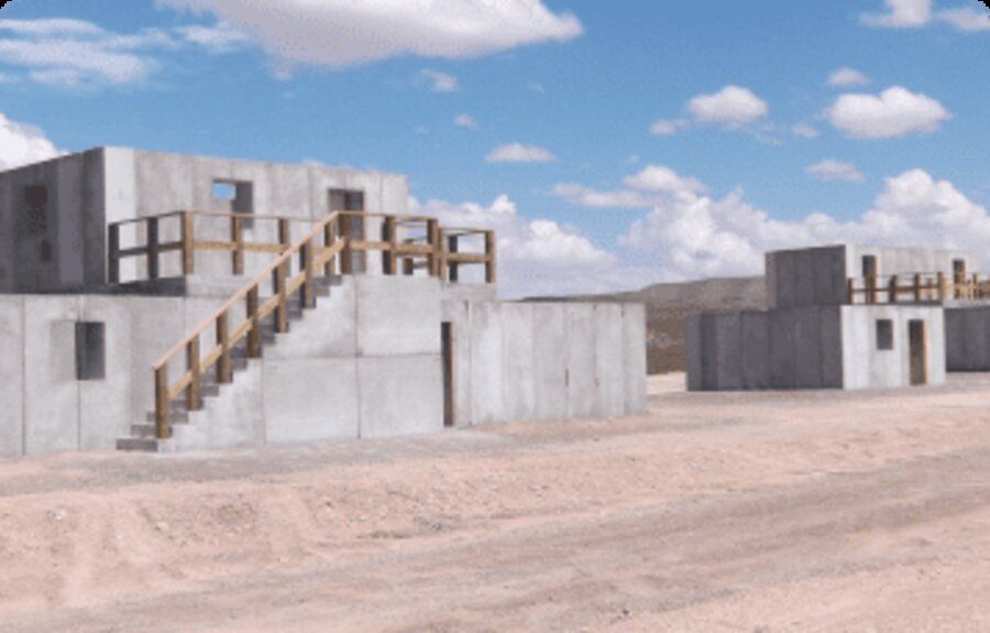 Aerial view of a live-fire training village with elevated wood staircases and second-story ballistic concrete structures