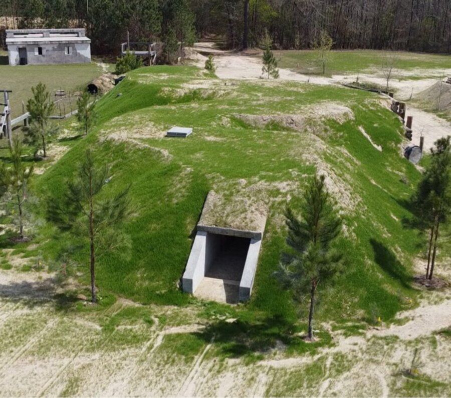 Aerial view of an earth-covered subterranean live-fire training facility with a concrete entry tunnel